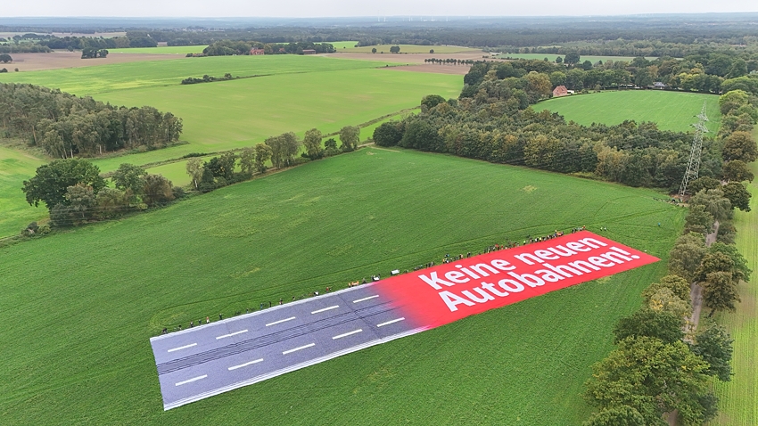 Banneraktion gegen die A39 am 01.10.2023: Das riesige Banner am Ort der geplanten Autobahn - tatsächlich noch viel breiter zerstört der Bau die Landschaft. Foto: Malte Hübner.