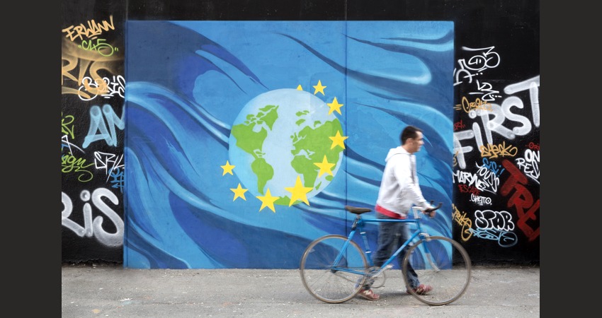 A man walking with a bike in front of a graffiti illustrating the 9th priority of the Juncker's Commission: "A stronger global actor", at an artist collectiv called Les Frigos, in the 13th Arrondissement of Paris, France. Graffiti, Paris 2015. Foto: Johanna Leguerre, Graffiti: Thomas Dechoux. European Union, 2015.