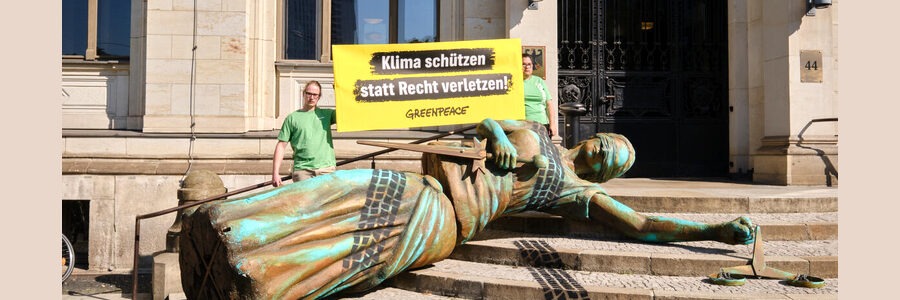 Foto: Pressefoto Greenpeace. Mit einer vier Meter großen, von Autospuren überfahrenen Justitia-Figur demonstrierten zwölf Greenpeace-Aktivist:innen am 15. Juli 2024 auf den Stufen zum Verkehrsministerium für grundrechtskonformen Klimaschutz im Verkehr. „Klima schützen statt Recht verletzen!“ Auch Greenpeace wird sich an der Verfassungsbeschwerde für ausreichenden Klimaschutz auch im Verkehrssektor beteiligen.