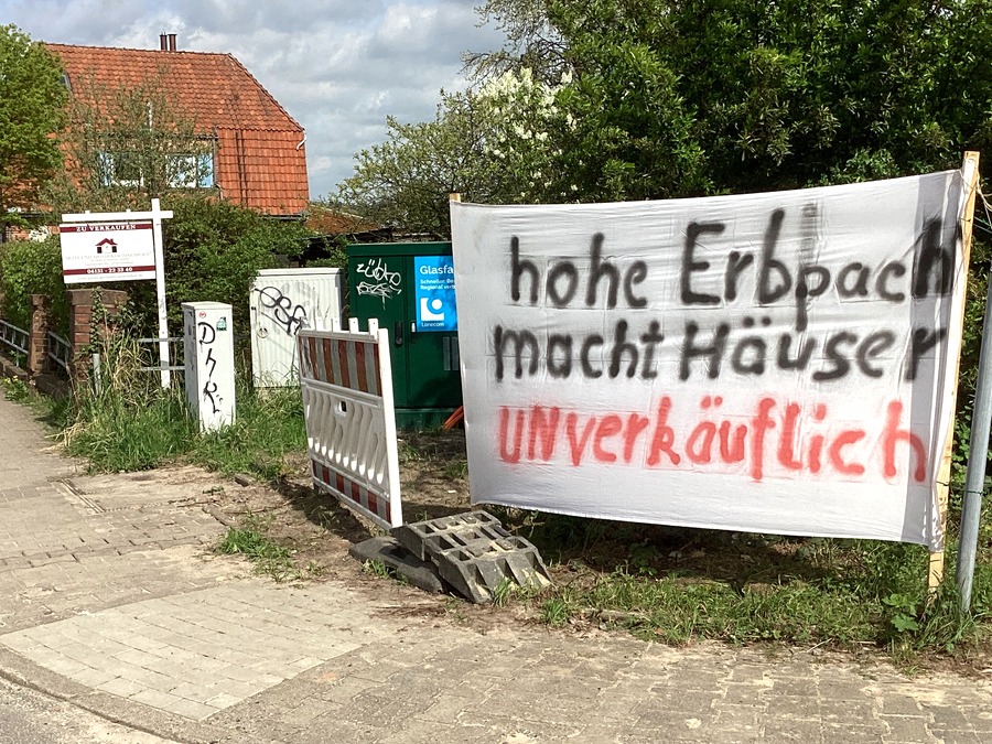 Initiative "Bezahlbarer Wohnraum im Erbbau Lüneburg": Hohe Erbpacht macht Häuser unverkäuflich. Banner an der Gartenhecke eines Hauses in Lüneburg.