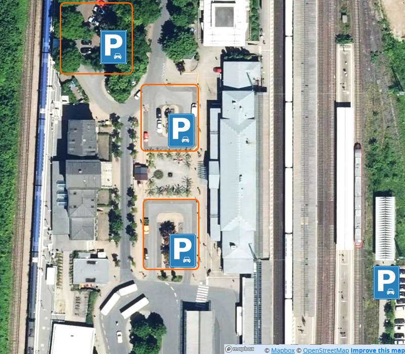 Bahnhofsbereich mit Kfz-Parkplätzen. Luftbild: Mapbox Satellite.