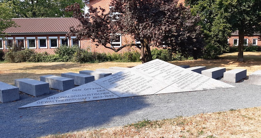 Foto: Lüne-Blog. Mahnmal für die Opfer des Nationalsozialismus, Lindenstraße, Lüneburg. Das Mahnmal wurde 1990 eingeweiht. Die 13 Quader mit den Jahreszahlen 1933-1945 erinnern an Lagerblocks oder Sarkophage, der Winkel an Abzeichen, die KZ-Gefangene an der Kleidung trugen.