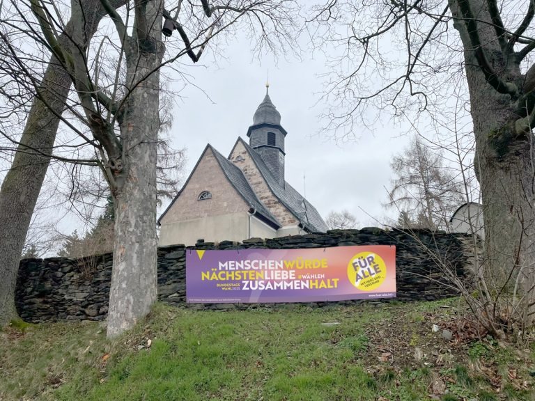 Banner an der Mauer des Friedhofs. Foto: Initiative „Für alle. Mit Herz und Verstand“ von evangelischer und katholischer Kirche in Deutschland.