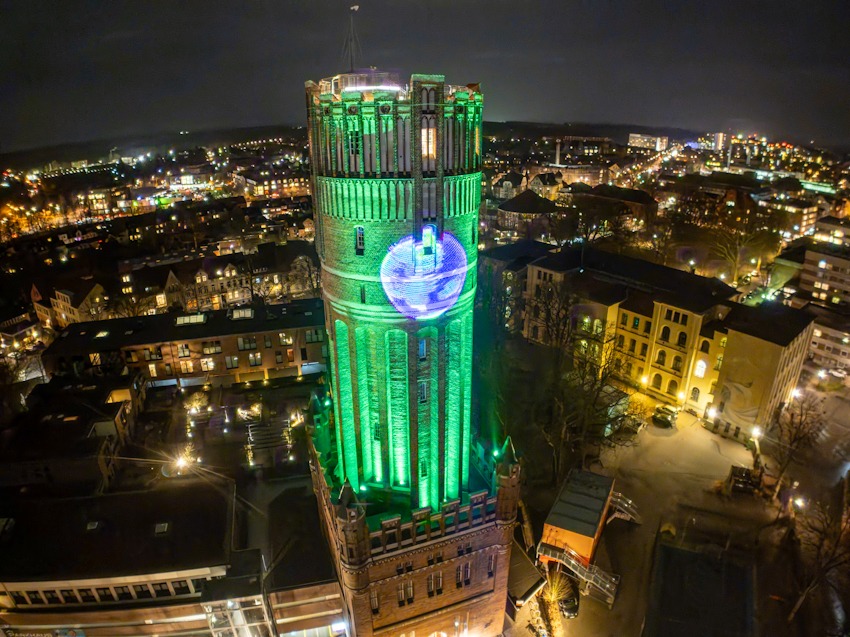 Foto: Lünedrohne. Beleuchteter Wasserturm in Lüneburg mit dem Logo von Fridays for Future. 