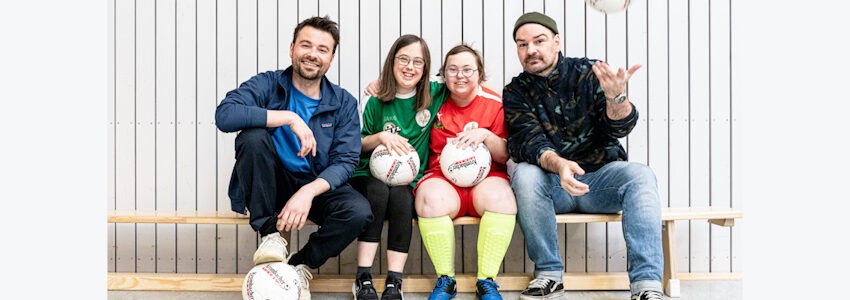 Foto: Lebenshilfe Lüneburg-Harburg. Von Down-Syndrom betroffene Sportlerinnen warten auf den Start ihres Fußballspiels. Rechts von ihnen sitzt der Fotograf Mathias Mensch, links Tomasz Ziolkowski, von der Lebenshilfe Lüneburg-Harburg.