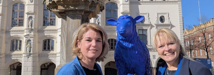 Lüneburgs Oberbürgermeisterin Claudia Kalisch (l.) und Melanie-Gitte Lansmann, Geschäftsführerin der Lüneburg Marketing GmbH, mit einem der Schafe aus der blauen Friedensherde. Foto: Hansestadt Lüneburg