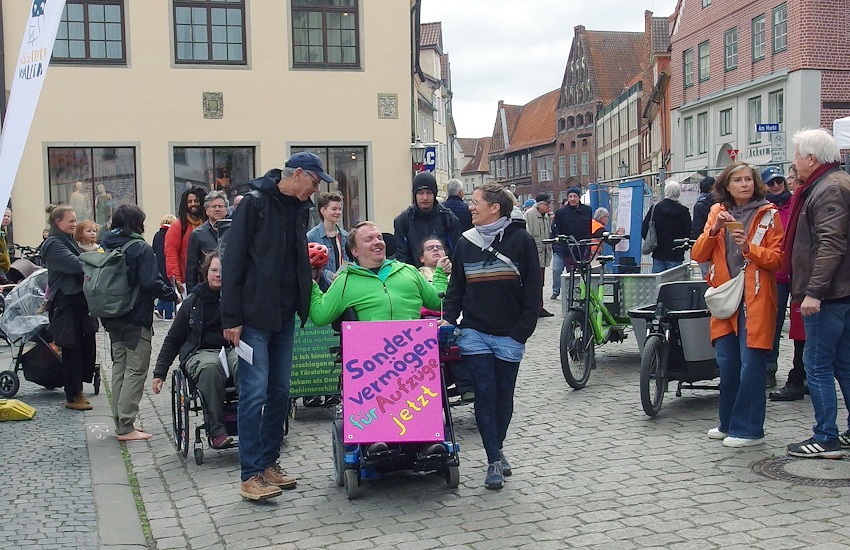 Foto: AAA LG. Rollifahrer mit dem Plakat "Sondervermögen für Aufzüge - jetzt!" Protestzug der Antiableistischen Aktion Lüneburg am 4. Mai 2025 auf dem "Markt der Inklusion".