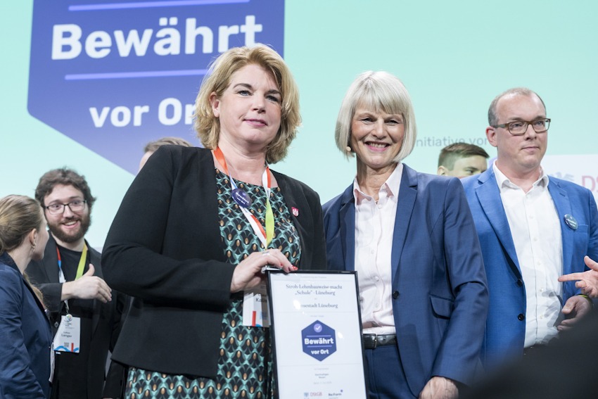 Foto: Henning Angerer/ DStGB. Im Rahmen des Deutschen Kommunalkongresses 2025 in Berlin am 3. Juni 2025 erhält Lüneburgs Oberbürgermeisterin Claudia Kalisch das Siegel „Bewährt vor Ort“ von Moderatorin Gundula Gause.