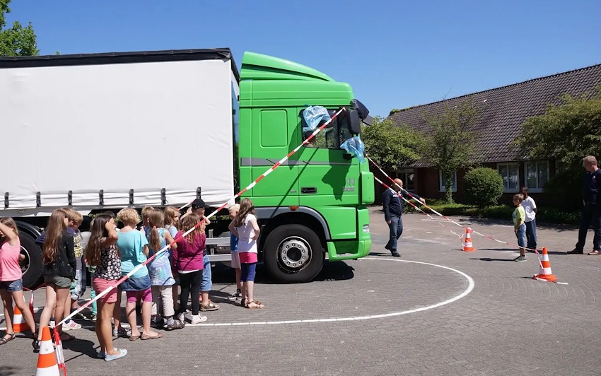 Aufklärungsaktion zum Thema Toter Winkel: Der Tote Winkel vor und neben dem Lkw ist mit Flatterband markiert. Kinder einer Grundschule haben sich in diesem Bereich aufgestellt. Der Round Table Ammerland in Niedersachsen macht mit dieser Aktion auf das Problem aufmerksam. Foto: Fahrradmagazin.net (https://www.fahrradmagazin.net/ratgeber/projekt-toter-winkel/).
