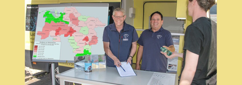 Matthias Ahlbrecht und Frank Sombrowski nehmen die Wasserprobe eines Brunnenbesitzers entgegen. Links die Nitratkarte vom Landkreis Lüneburg. Foto: Harald Guelzow.