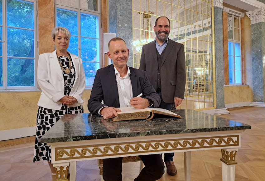 Foto: Christian Ratzel / Stadt Köthen (Anhalt). Stadtrat Matthias Rink (M.) trug sich unter den Augen von Köthens Oberbürgermeisterin Christina Buchheim für die Hansestadt Lüneburg im Köthener Schloss ins Goldene Buch der Stadt Köthen (Anhalt) ein. Rechts: Sven Lucht, stellvertretender Bürgermeister der Stadt Langenfeld, mit der Köthen ebenfalls eine Städtefreundschaft pflegt. 