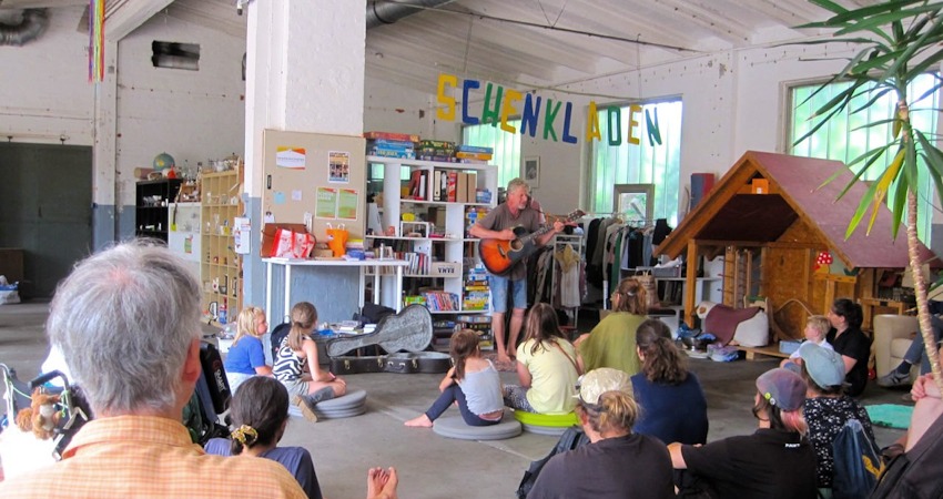 Foto: Commons Zentrum. Wohnzimmer-Konzert mit Song X am 29. Juni 2025. Im Hintergrund der Schenkladen. Hier kann man kostenlos einstellen und mitnehmen. 