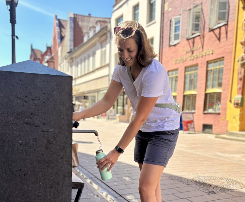 Foto: Hansestadt Lüneburg. Klimaanpassungsmanagerin Amelie Grunenberg an einem Trinkwasserspender in Lüneburg, der ebenfalls in der aktuellen Hitzekarte zu finden ist.