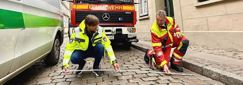 Fotos: Hansestadt Lüneburg. 2,20 Meter Durchfahrtsbreite messen Thorsten Diesterhöft, Leiter der ersten Wachabteilung der Hauptberuflichen Wachbereitschaft (rechts) und Dennis Lauterschlag, Leiter des Bereichs Ordnung und Verkehr in der Unteren Ohlinger Straße neben einem parkenden Auto – deutlich zu wenig, um mit einem Einsatzfahrzeug zu passieren.