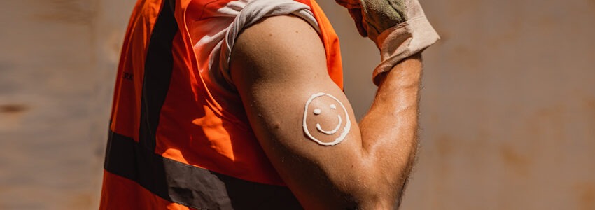 Foto: IG BAU | Nils Hillebrand. Sonnenschutz ist sexy. Gebräunter Mann mit Creme-Smiley am Oberarm.