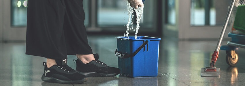 Foto: IG BAU. Putzlappen wird über einem Wischeimer ausgewrungen.