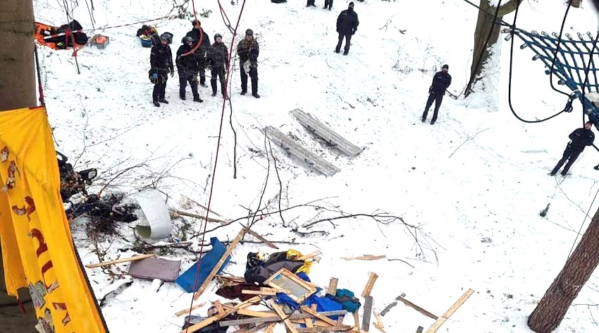 Foto: KlimaKollektiv. Polizisten stehen vor am Boden liegende Bauteile eines Baumhauses im Lüner Holz am 12.01.2026.
