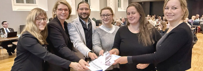 Foto: Hansestadt Lüneburg. Von links: Eva Kern, Koordinatorin des Bürger:innenrats, Oberbürgermeisterin Claudia Kalisch, die Mitglieder des Bürger:innenrats 2025, Tommy Ziegler, Josefina Budzisch und Franziska Hartmann und - ganz rechts - Bürgermeisterin Jule Grunau mit dem aktuellen Bürgergutachten am 12. Februar 2026.