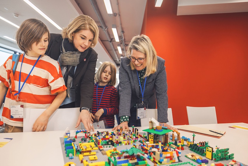 Foto: Leuphana Media Studio. Oberbürgermeisterin Claudia Kalisch und Jutta Bauer (rechts), Fachbereichsleiterin Bildung bei der Hansestadt, lassen sich von den Kindern ihre Wunschschule aus Lego erklären. Bildungskonferenz am 17. Februar 2026.