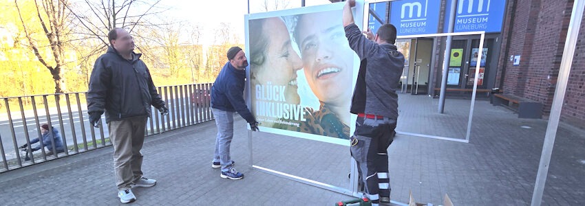 Foto: Lüne-Blog. Mathias Mensch (Mitte) mit Kollegen beim Aufbau der Sonderausstellung „Glück inklusive – Unser Leben mit Behinderung“ vor dem Eingang zum Museum Lüneburg.