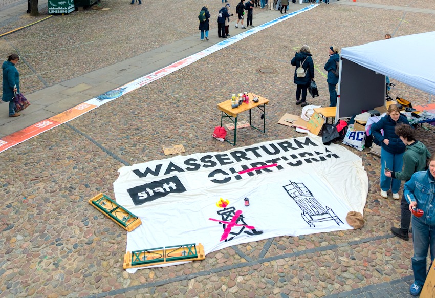 Foto: Malte Hübner. Luftbild des Klimazeitstrahls auf dem Marktplatz in Lüneburg am 24. April 2026. Rechts im Vordergrund der Stand von Fridays for Future. Die Initiative gestaltete am Vormittag ein Transparent zum Protest gegen die von der Bundesregierung geplanten Rückschritte bei der Energiewende. Noch fehlt das "B" für "Bohrturm".