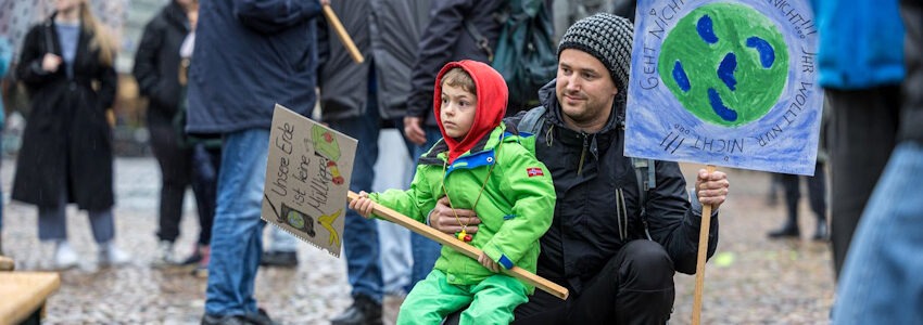 Foto: Malte Hübner. Ein Vater protestiert mit seinem Kind am 14. November 2025 auf dem Marktplatz in Lüneburg für Klimaschutz.