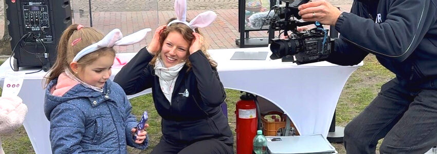 Foto: Stadtmarketing Uelzen. Osteraktion 2026: Das kleine Mädchen hat die Ausbildung als Osterhase bestanden und erhält die Urkunde und Schokohasen zur Belohnung.