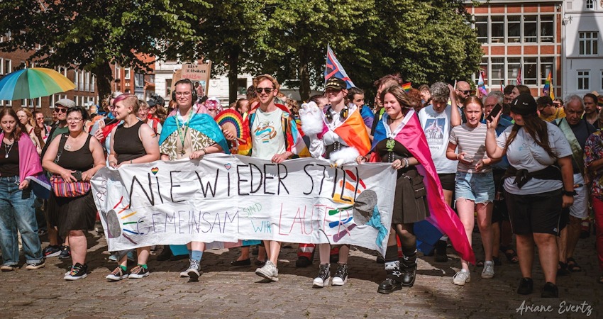Foto: Ariane Evertz. Pride-Demonstration auf dem Marktplatz in Lüneburg mit Banner: Nie wieder still!