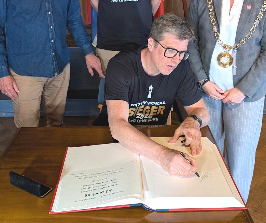 Foto: Hansestadt Lüneburg. Beim Empfang im Rathaus trug sich die gesamte Mannschaft der SVG Lüneburg unter den Augen von Oberbürgermeisterin Claudia Kalisch ins Ehrenbuch der Hansestadt ein. Cheftrainer Stefan Hübner macht hier den Anfang. 