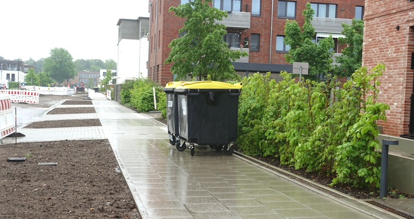 Foto: Uwe Wenk, 11.05.2026. Gehweg an der Lübecker Straße.
Positiv: Eine angenehm begeh- und befahrbare Oberfläche für Gehhilfen.
Aber: Die Standard-Gehwegbreite beträgt 2,50 Meter. Dann können zwei Menschen bequem nebeneinander und aneinander vorbei gehen. Obwohl hier genügend Platz nach links wäre, ist der Gehweg hier aber nur 2 Meter breit. Zudem ist er zugestellt mit Müllcontainern. Für Fußgänger bleiben nur noch etwa 1,20 Meter - für den Rollstuhl zu knapp.