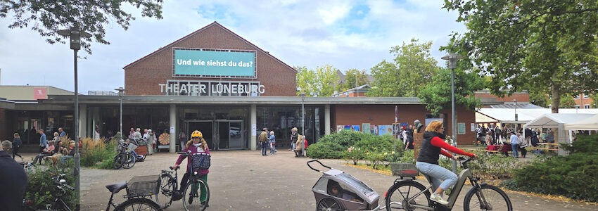 Foto: Lüne-Blog. Eingangsbereich des Theaters Lüneburg beim Theaterfest zur Saisoneröffnung am 30. August 2026. Rechts sind Veranstaltungszelt und Stände zu erkennen. Motto der diesjährigen Spielzeit: „Und wie siehst du das?“