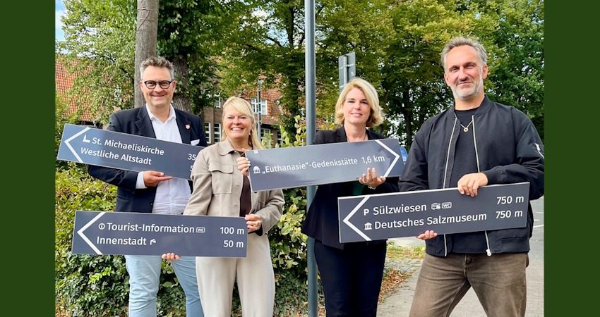Foto: Hansestadt Lüneburg. Von links: Stabsstellenleiter Carl-Ernst Müller, Melanie-Gitte Lansmann (Lüneburg Marketing), Oberbürgermeisterin Claudia Kalisch und Mathias Schneider aus dem Team Strategische Innenstadtentwicklung mit den ersten Schildern, die am Marienplatz angebracht wurden.